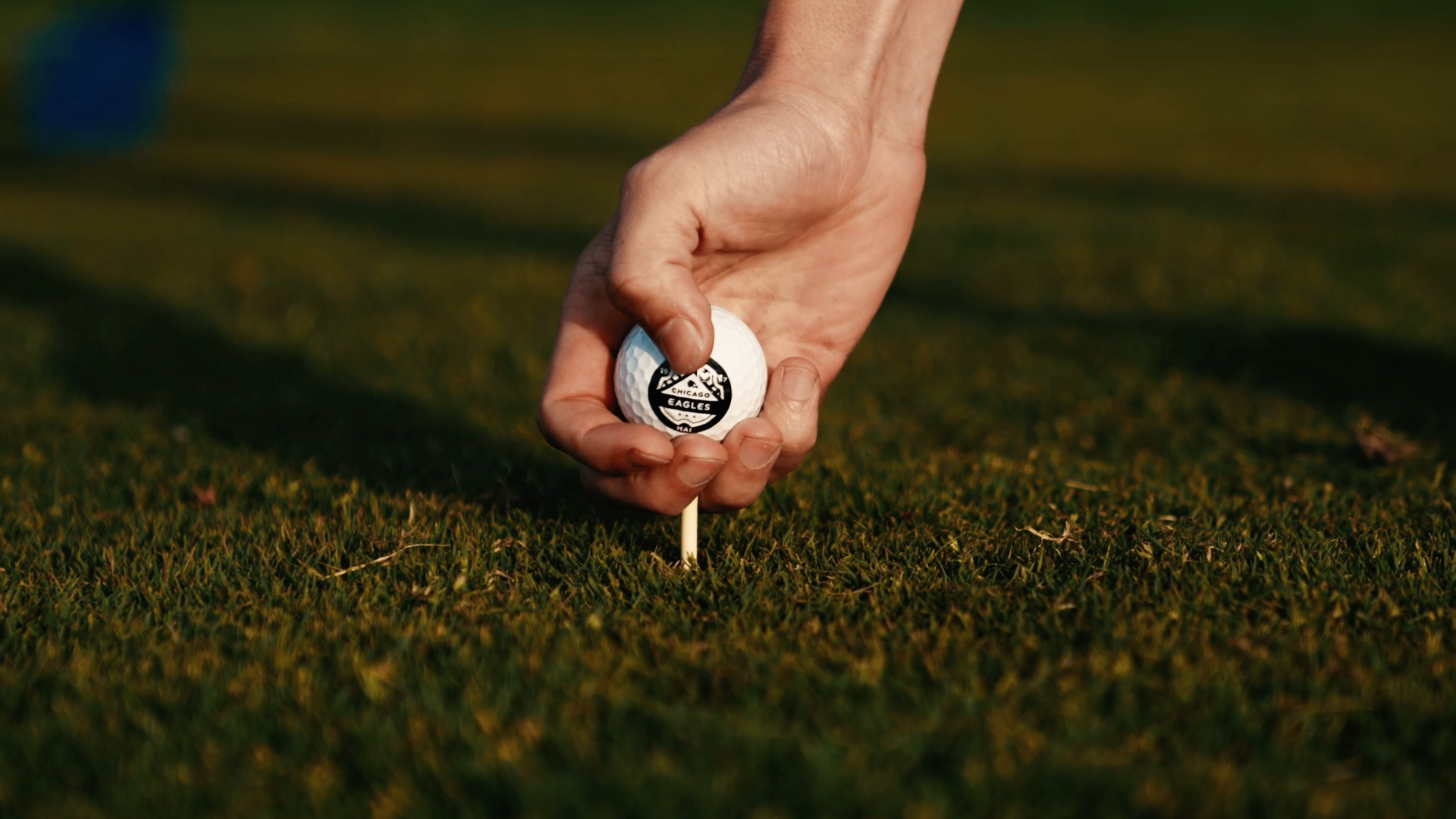 Hand placing a Chicago Eagles golf ball on a tee